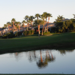 A view across a calm lake at the golf course and residences that flank it. 
