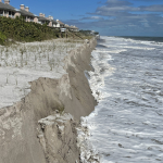 A portion of dune collapses, as ocean water pounds at its base.