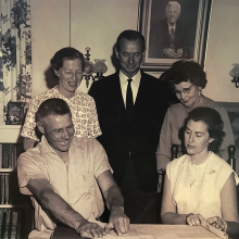 Members of the Town's first Council gather around the top-end of a dining table looking at a map