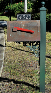Letter box by the side of the road in the grass with its flag down and number 452 on top.
