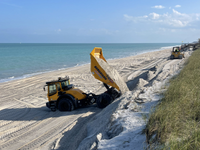 A dump truck deposits sand on the beach while a small excavator shapes the new dune.