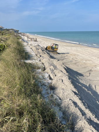 A piece of heavy equipment on the beach pushes sand up onto the dunes.