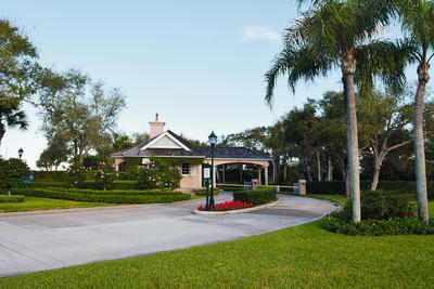 The entrance gatehouse surrounded by palm trees and hibiscus bushes while the entrance bars are closed.