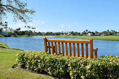 A wooden bench surrounded by bushes overlooks a golf course late surrounded by homes