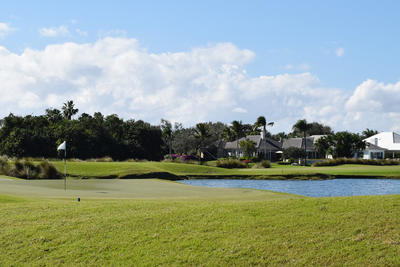 A golf course flag close to a lake with houses next to it