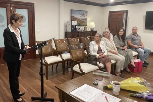 Florida Association of City Clerks President Patricia Burke stands at a podium in Town Hall beside members of the public.